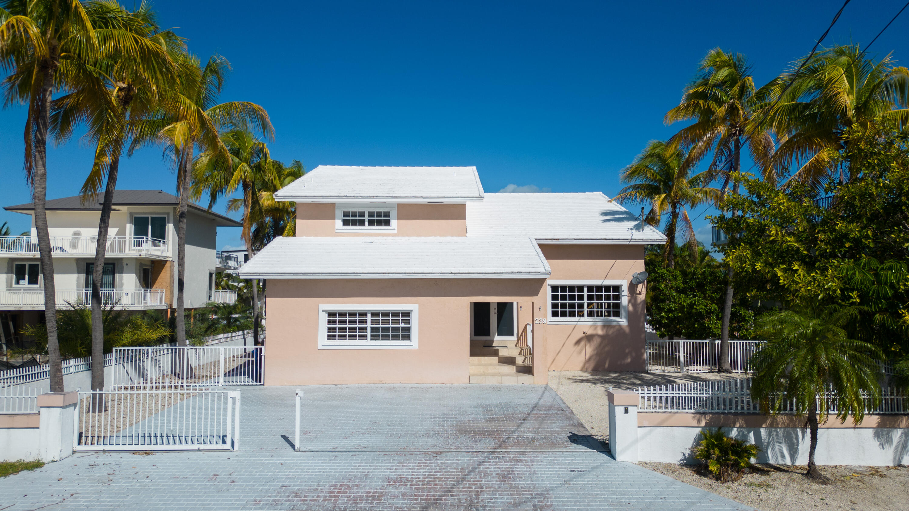 239 Atlantic Boulevard Key Largo, FL 33037 - Photo 3 of 50 a view of a white house with a yard and table and chairs under an umbrella