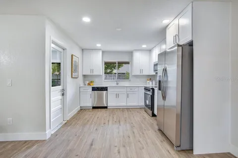 a kitchen with stainless steel appliances a refrigerator a sink dishwasher a stove and white cabinets with wooden floor