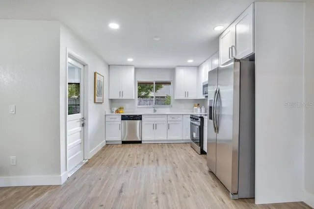 a kitchen with stainless steel appliances a refrigerator a sink dishwasher a stove and white cabinets with wooden floor