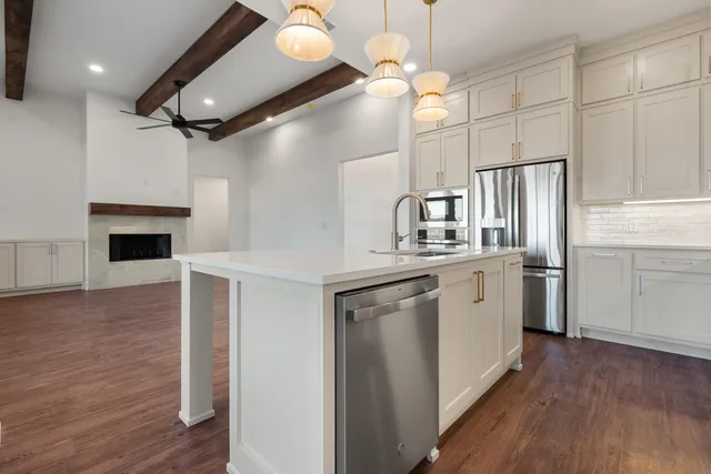 a kitchen with stainless steel appliances granite countertop a refrigerator a sink dishwasher a stove and white countertops with wooden floor