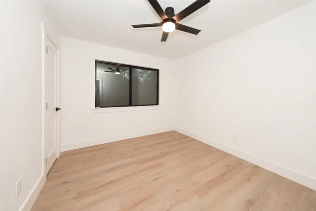 a view of an empty room with wooden floor and a ceiling fan