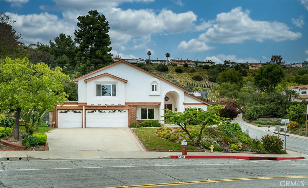 a view of a white house with a yard plants and large tree