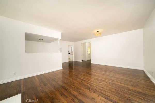 a view of empty room with wooden floor and kitchen