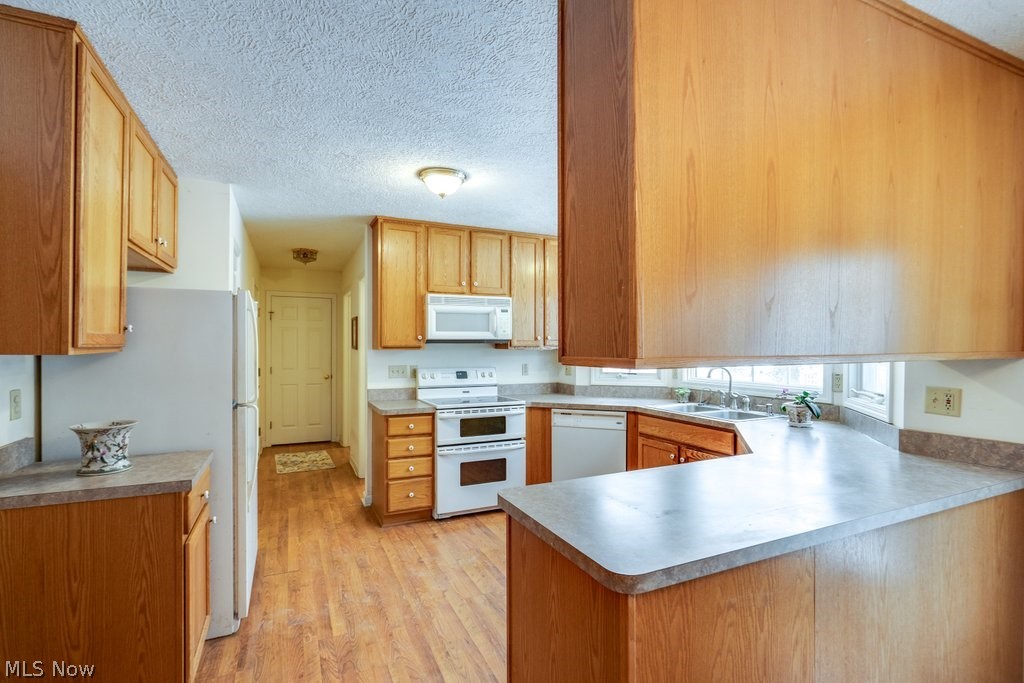 136 Taylor Road Barberton, OH 44203 - Photo 13 of 45 Kitchen with white appliances, a textured ceiling, light wood finished floors, a peninsula, and wood finish cabinetry