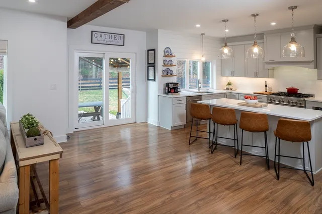 a kitchen with stainless steel appliances granite countertop a stove top oven a sink dishwasher and a dining table with wooden floor