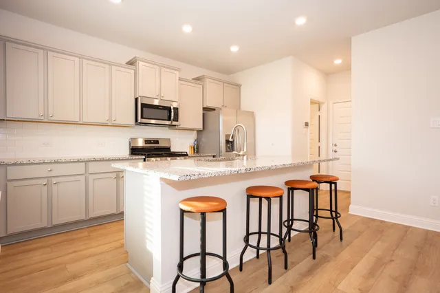 a kitchen with stainless steel appliances granite countertop a stove a sink a microwave a dining table and chairs with wooden floor