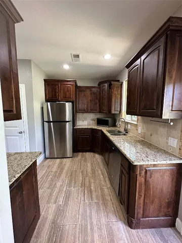 a kitchen with stainless steel appliances granite countertop a refrigerator a sink dishwasher a stove with wooden floors