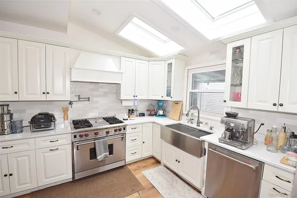 a kitchen with stainless steel appliances kitchen island granite countertop a refrigerator a sink dishwasher a stove and white cabinets with wooden floor