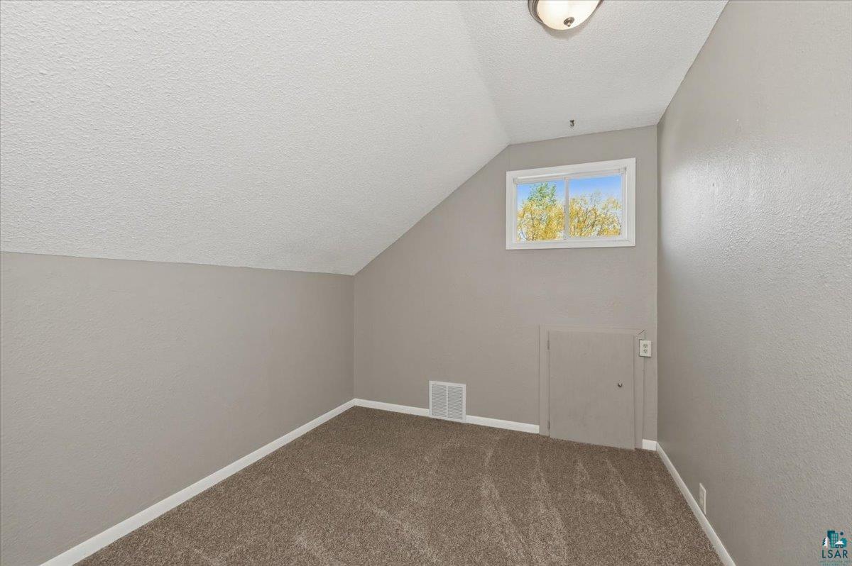 5319 East 3rd Street Superior, WI 54880 - Photo 24 of 33 Carpeted room featuring a white-trimmed window, sloped ceiling, and a flush-mounted ceiling light fixture