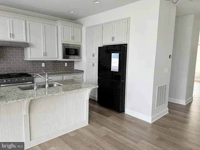 a kitchen with stainless steel appliances granite countertop a refrigerator stove a sink and white cabinets with wooden floor