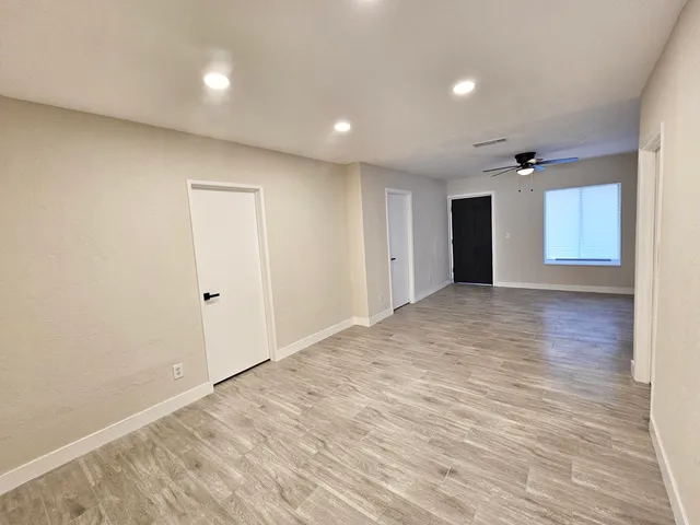 a view of an empty room with wooden floor and a ceiling fan