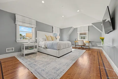 a spacious bedroom with a bed and a flat tv screen on the dresser