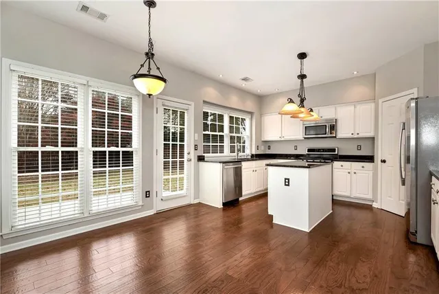 a kitchen with granite countertop a stove a sink dishwasher a refrigerator and white cabinets with wooden floor