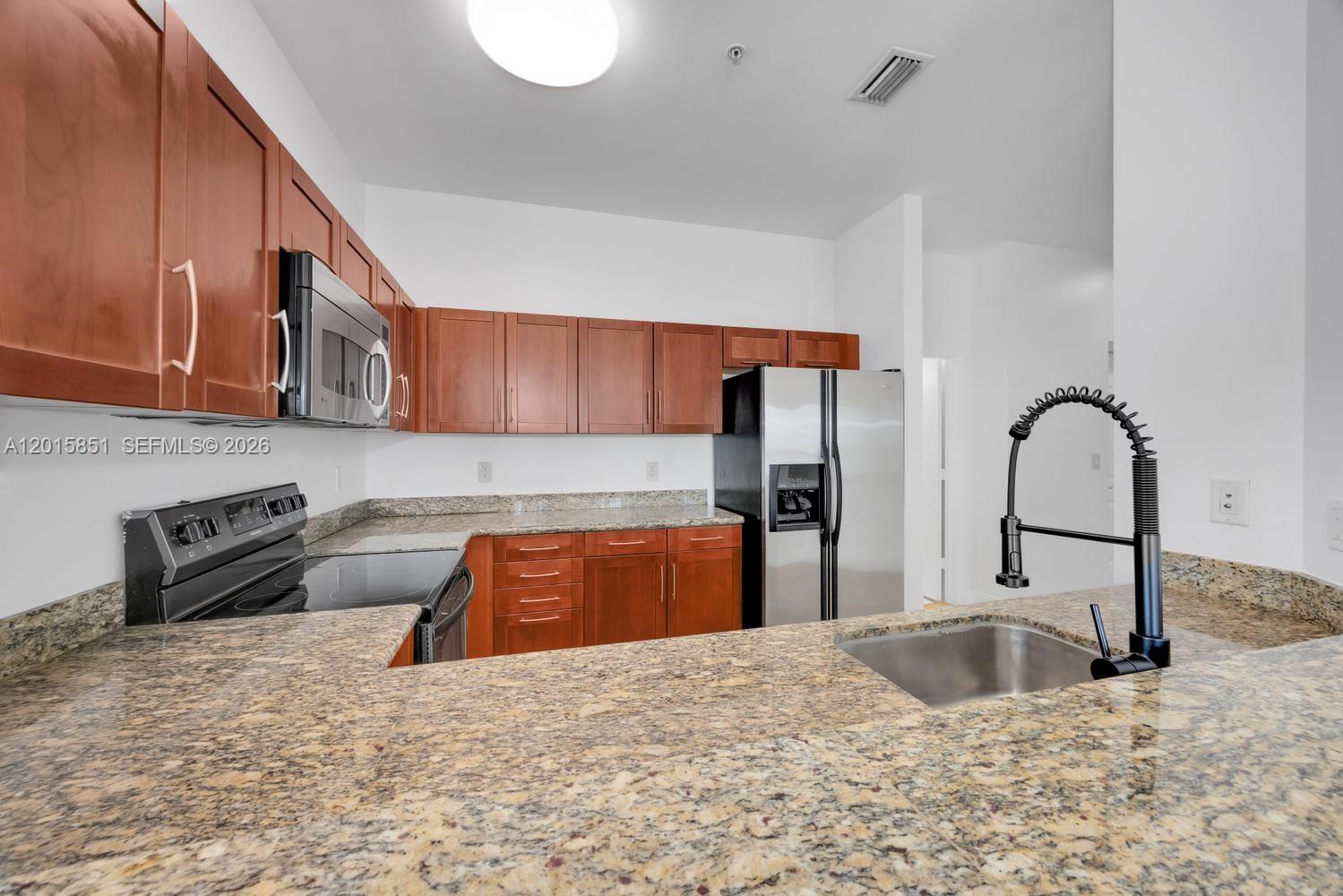 7275 Southwest 90th Street, Unit C719 Miami, FL 33156 - Photo 11 of 25 a kitchen with stainless steel appliances granite countertop a sink a stove and a wooden cabinets