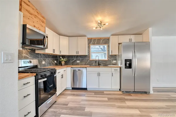 a kitchen with stainless steel appliances granite countertop a stove top oven a refrigerator and white cabinets with wooden floor