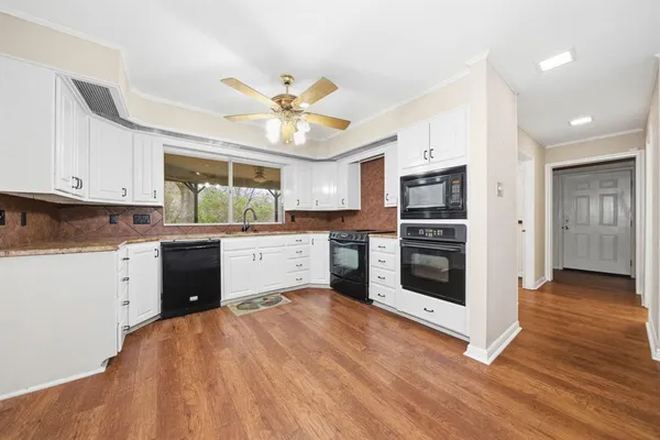 a kitchen with stainless steel appliances a stove a sink dishwasher a refrigerator with white cabinets and wooden floor