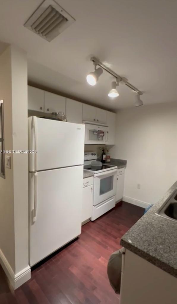 2740 Southwest 28th Terrace, Unit 503 Miami, FL 33133 - Photo 4 of 19 a kitchen with granite countertop a refrigerator a stove a sink and white cabinets with wooden floor