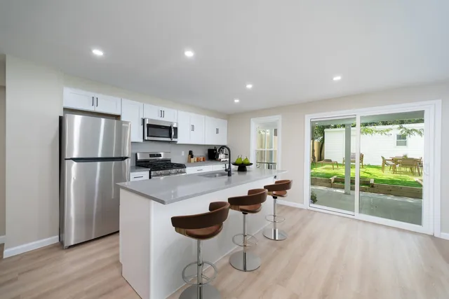 a kitchen with a refrigerator a microwave oven a sink and a dining table with wooden floor