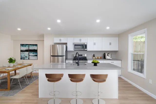 a kitchen with stainless steel appliances granite countertop a stove top oven a sink a refrigerator and white cabinets with wooden floor