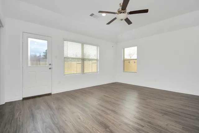 an empty room with wooden floor ceiling fan and windows