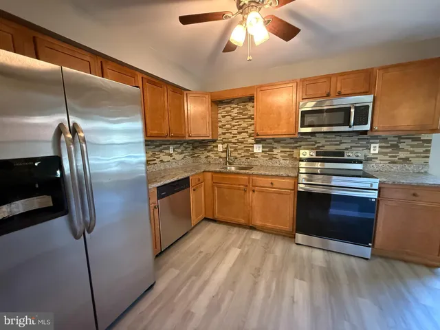 a kitchen with stainless steel appliances granite countertop a refrigerator a sink a stove top oven a washer dryer and cabinets