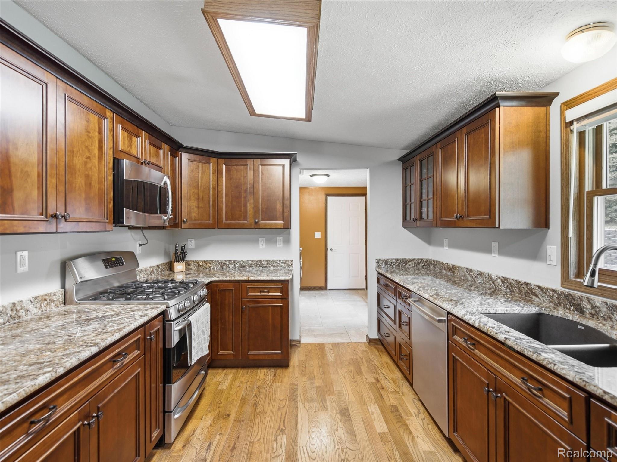 5003 Mason Road Howell, MI 48843 - Photo 12 of 59 Kitchen featuring wood-finish flooring, dark wood cabinetry, light-toned countertops, stainless steel appliances, and a double basin sink