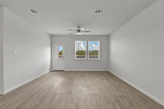 an empty room with wooden floor chandelier fan and windows