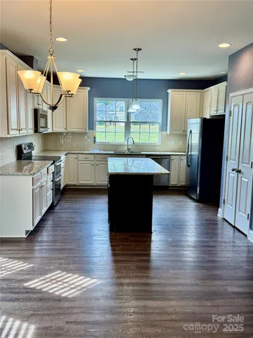 a kitchen with stainless steel appliances granite countertop a refrigerator a sink dishwasher a stove and white cabinets with wooden floor