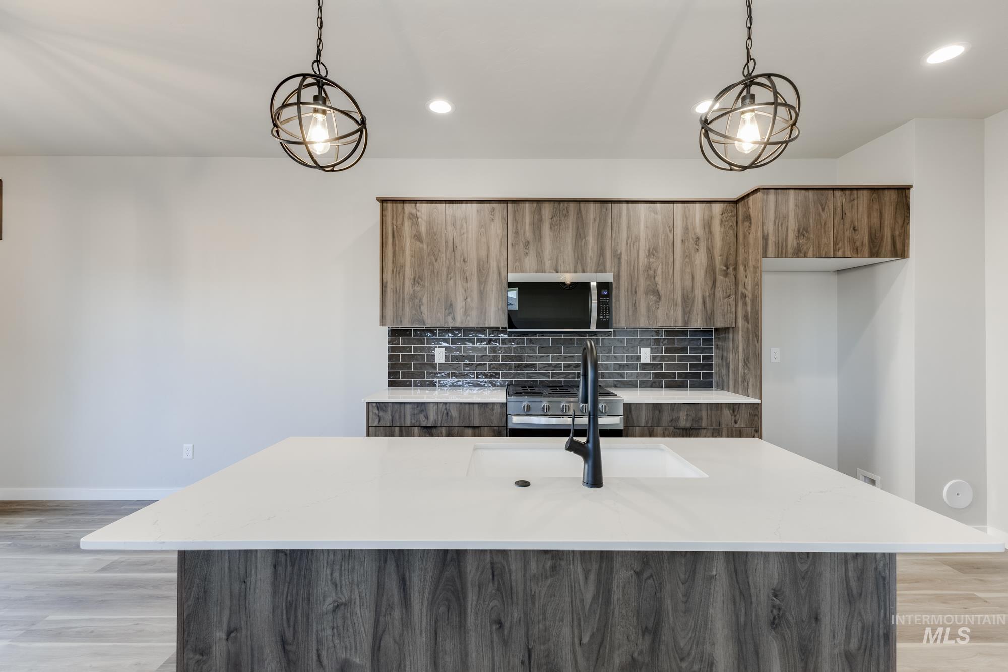 10574 West Teratai Street Star, ID 83669 - Photo 4 of 23 Kitchen featuring brown cabinets, light stone countertops, light wood-style floors, tasteful backsplash, and a center island with sink