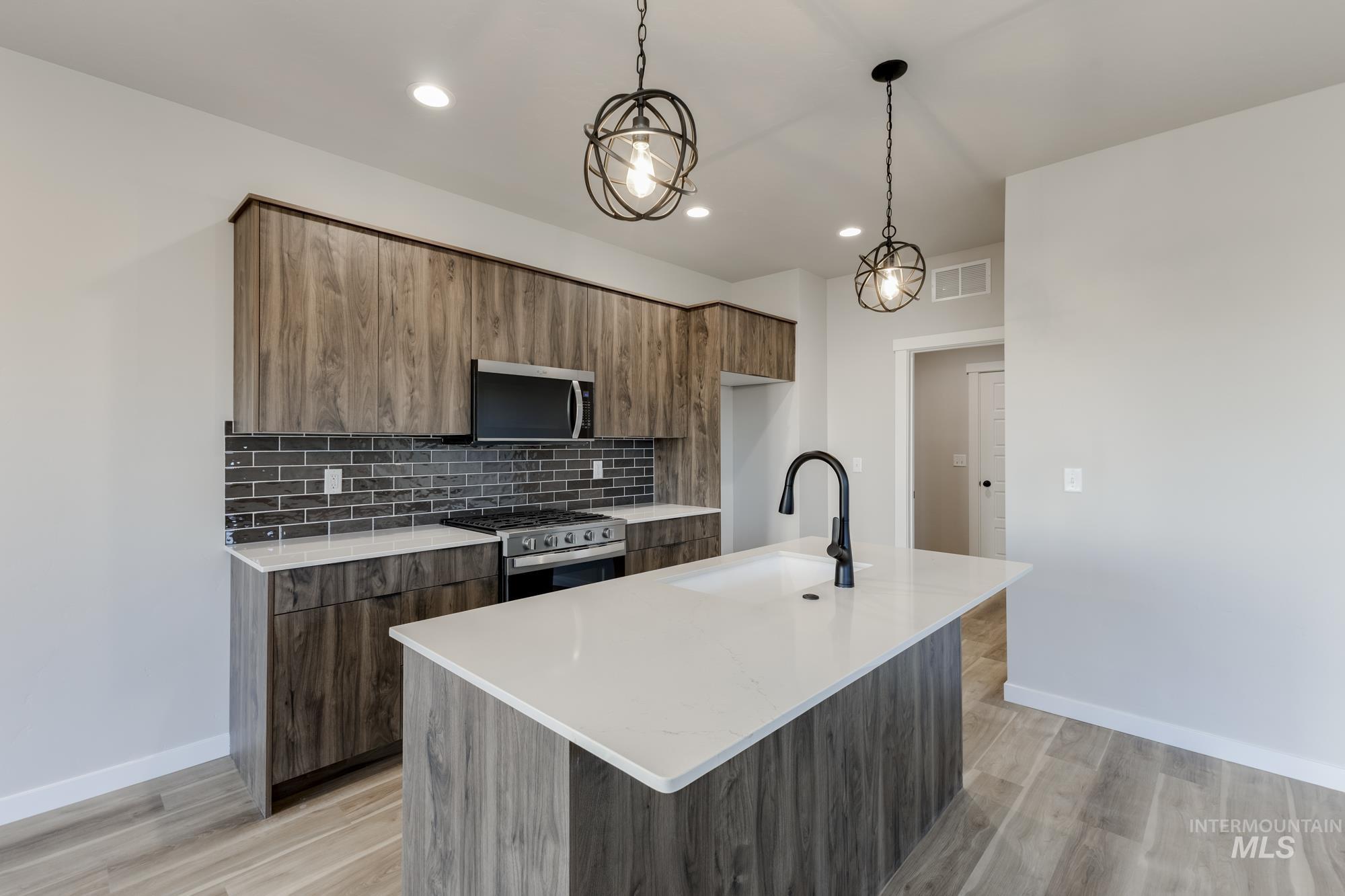 10574 West Teratai Street Star, ID 83669 - Photo 5 of 23 Kitchen with modern cabinets, a kitchen island with sink, light stone counters, tasteful backsplash, and appliances with stainless steel finishes