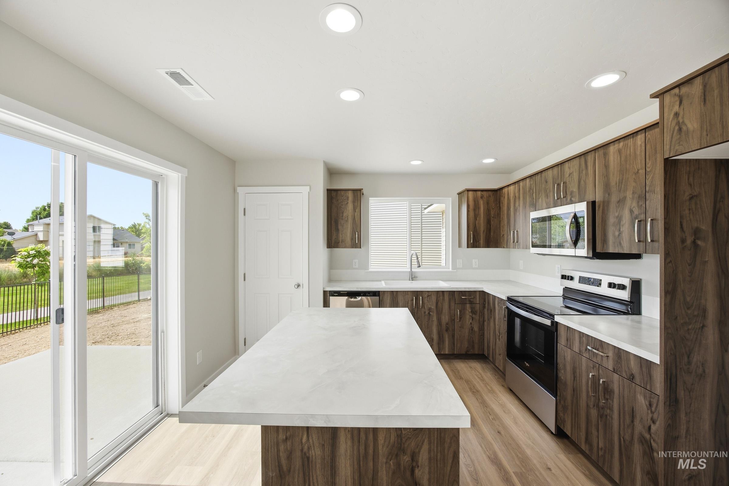 14044 Shiny Spruce Street Caldwell, ID 83607 - Photo 4 of 24 Modern kitchen featuring wood-finish cabinetry, light-toned countertops, stainless steel appliances, recessed lighting, and wood-finish flooring