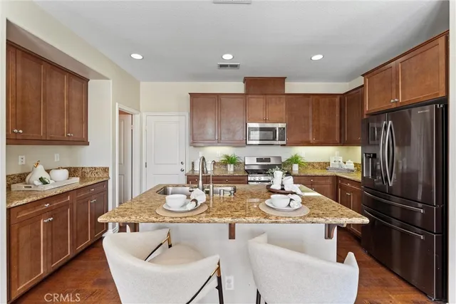 a kitchen with stainless steel appliances granite countertop a refrigerator a stove a sink a dining table and chairs with wooden floor