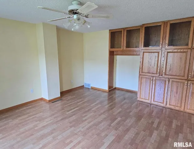 an empty room with wooden floor fan and windows