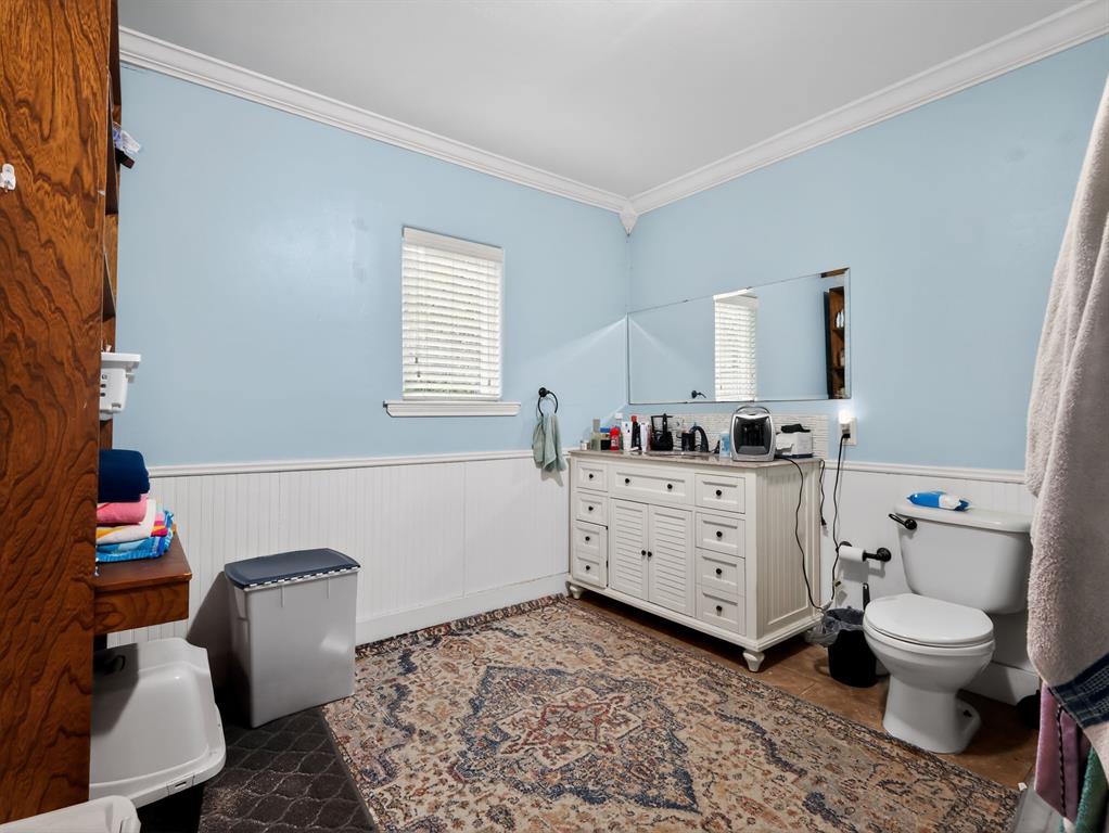 1301 Locust Street Commerce, TX 75428 - Photo 10 of 17 a room with a baby crib furniture a mirror and a toilet