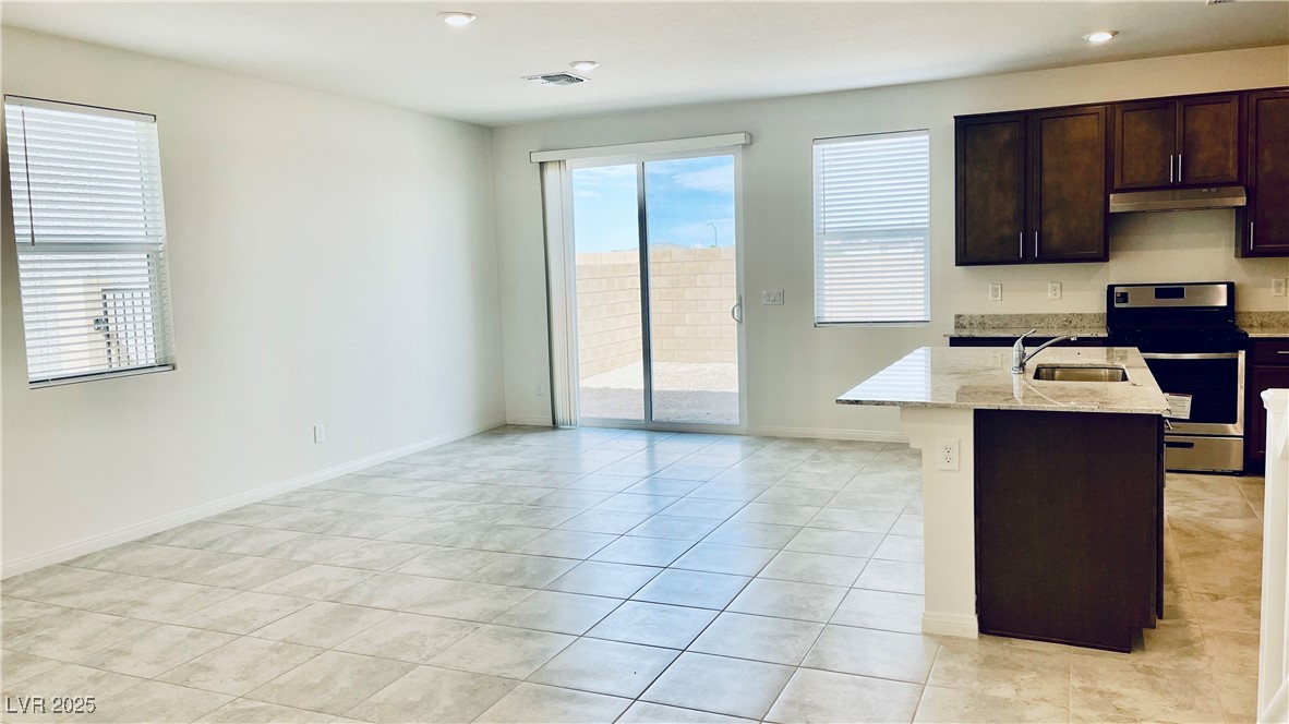 8736 Victoria Pk Street Las Vegas, NV 89148 - Photo 3 of 35 Kitchen with stainless steel electric range, dark brown cabinets, light stone countertops, a kitchen island with sink, and light tile patterned flooring