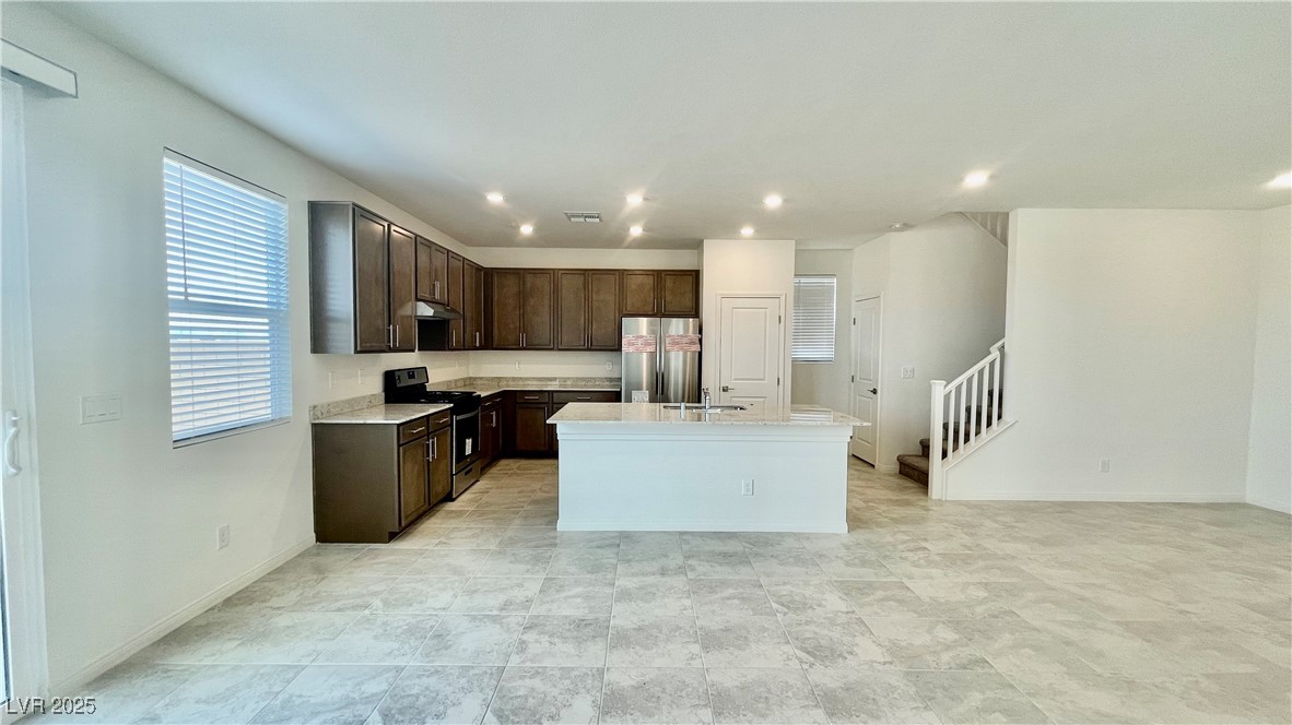 8736 Victoria Pk Street Las Vegas, NV 89148 - Photo 4 of 35 Kitchen featuring dark brown cabinetry, stove, freestanding refrigerator, a center island with sink, and light stone counters
