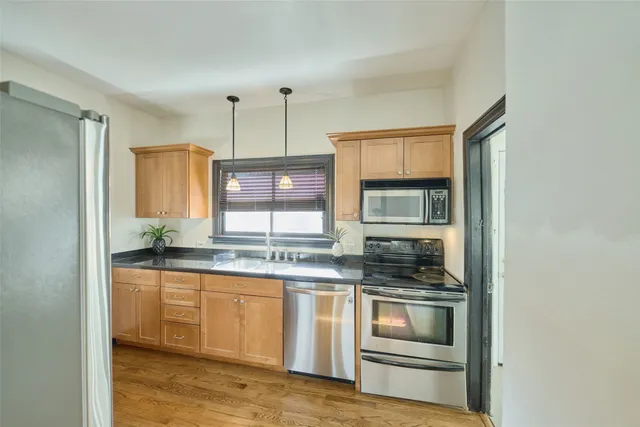 a view of a brick house in front of a yard with plants and large trees