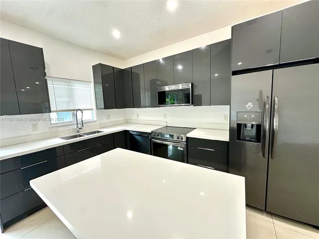 a large white kitchen with a large counter top space a sink stainless steel appliances and cabinets