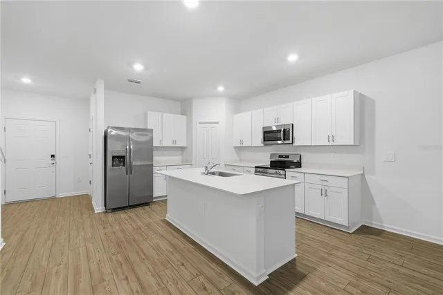 a kitchen with stainless steel appliances a refrigerator stove a sink and white cabinets with wooden floor