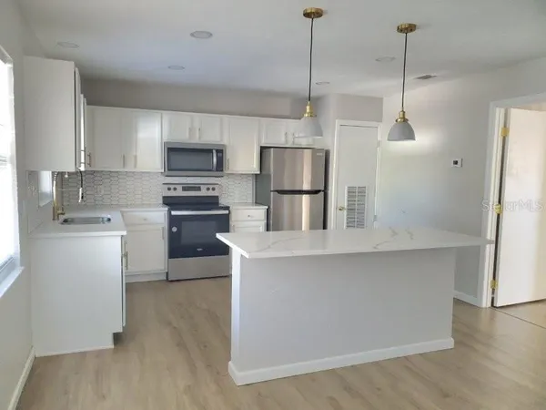 a kitchen with kitchen island a white counter top space stainless steel appliances and cabinets