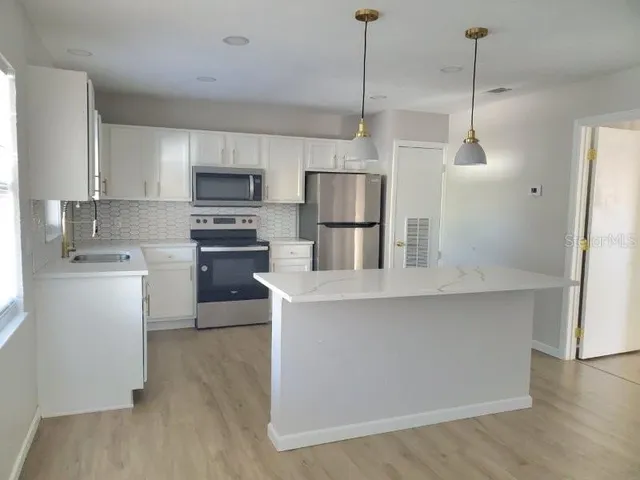 a kitchen with kitchen island a white counter top space stainless steel appliances and cabinets