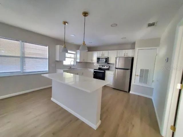 a kitchen with stainless steel appliances a refrigerator a sink dishwasher a stove and white countertops with wooden floor