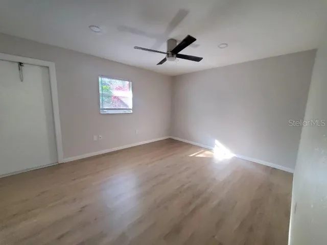 an empty room with wooden floor ceiling fan and windows