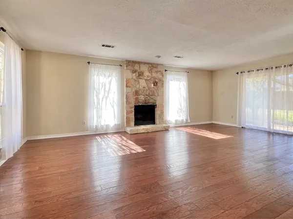 an empty room with wooden floor fireplace and windows