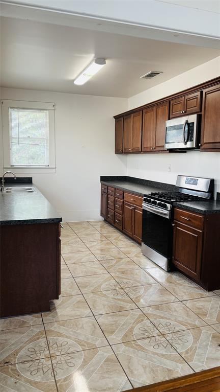 4616 Eastside Avenue, Unit A Dallas, TX 75226 - Photo 6 of 18 Kitchen with dark countertops, appliances with stainless steel finishes, dark brown cabinets, and light tile patterned floors