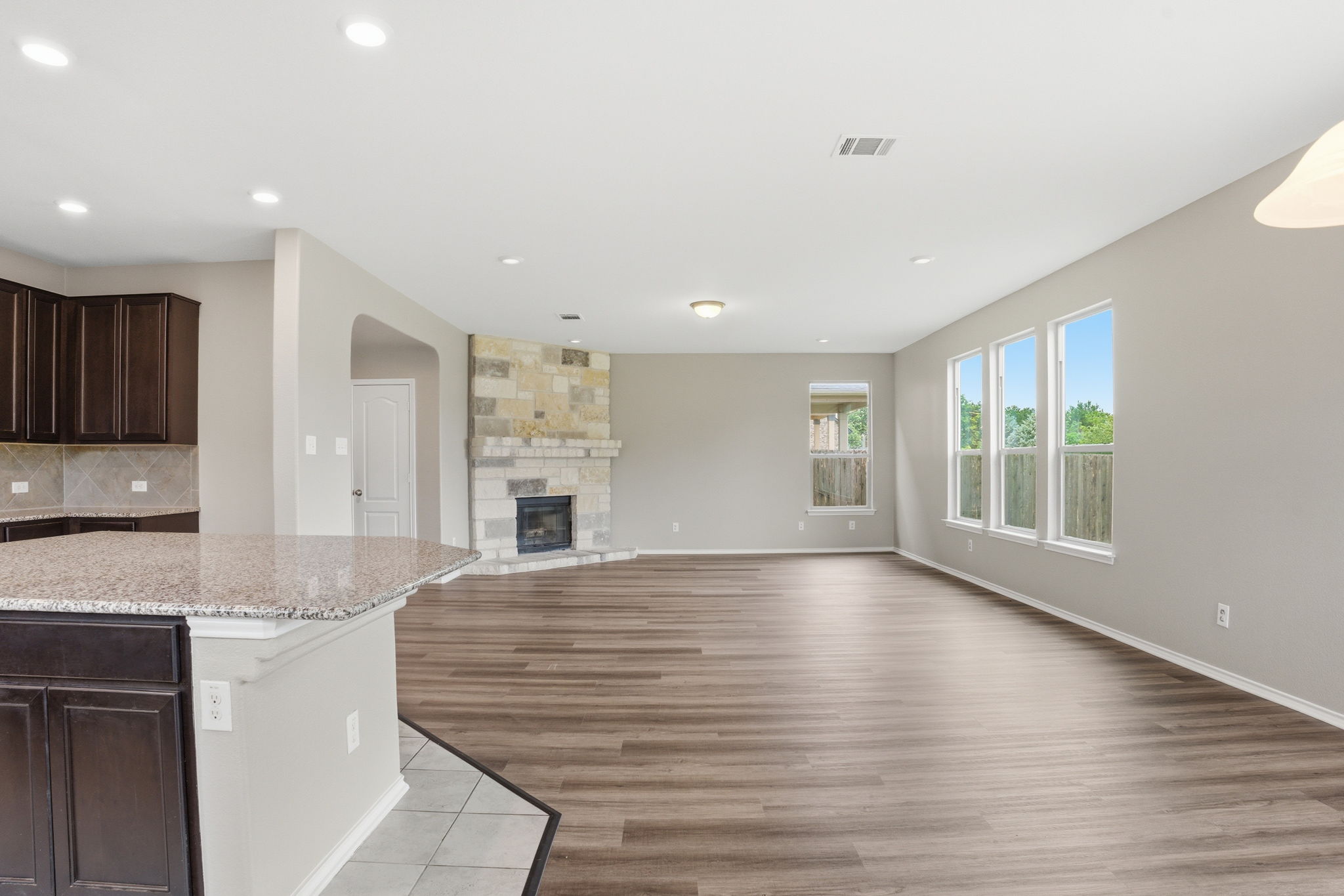 670 Landon Samuel Loop Pflugerville, TX 78660 - Photo 5 of 22 Spacious living area featuring wood-finish flooring, a stacked stone fireplace, and multiple windows