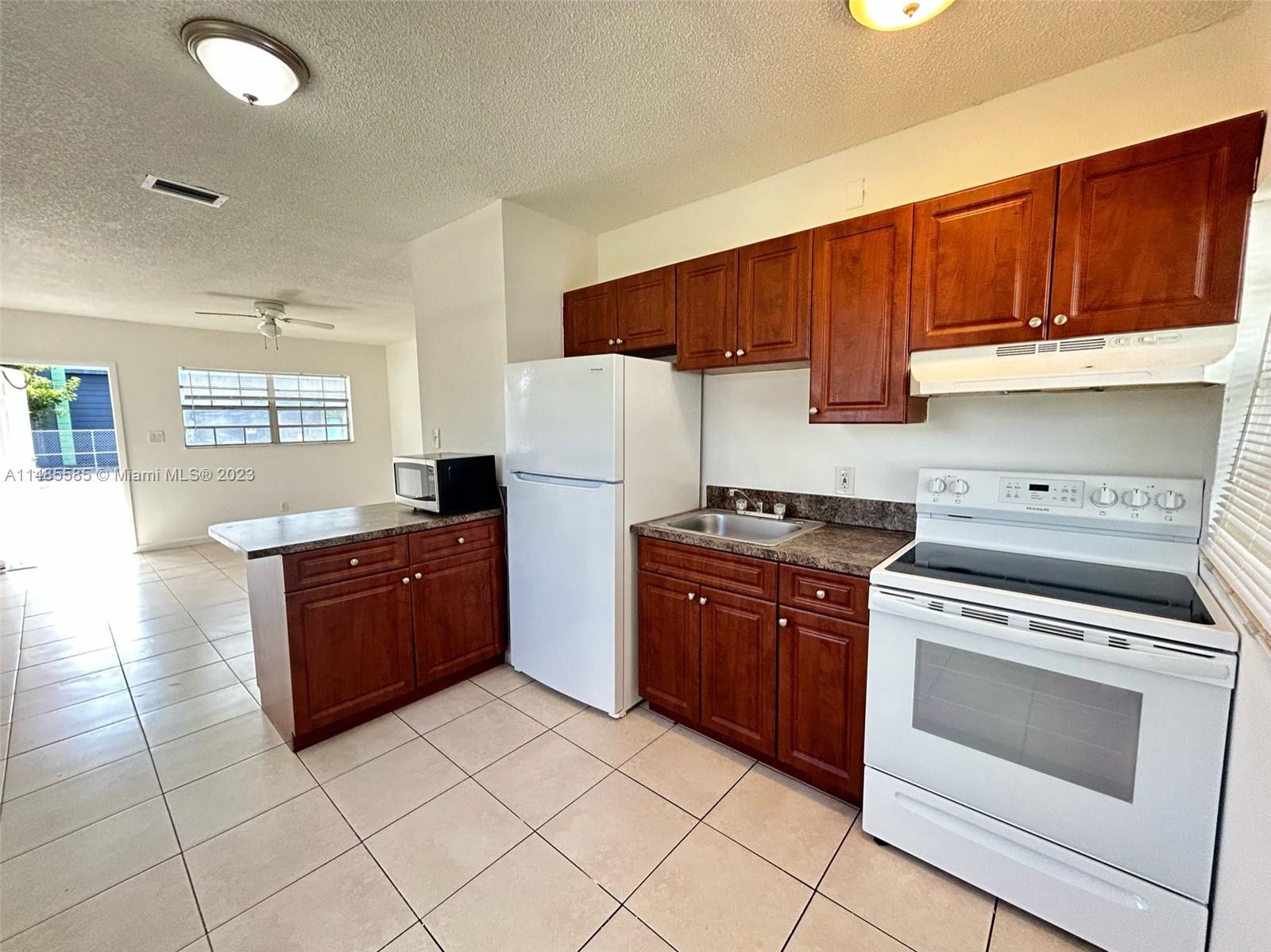 990 Phippen Waiters Road, Unit 1 Dania Beach, FL 33004 - Photo 7 of 8 a kitchen with stainless steel appliances granite countertop a stove top oven a sink dishwasher and a refrigerator with wooden cabinets