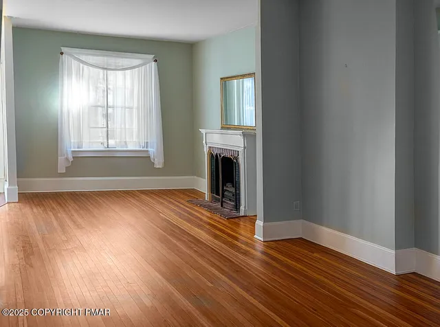an empty room with wooden floor fireplace and windows