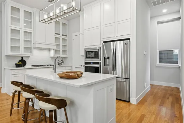 a white kitchen with stainless steel appliances granite countertop a stove a sink a refrigerator and white cabinets with wooden floor