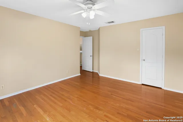 an empty room with wooden floor chandelier fan and windows